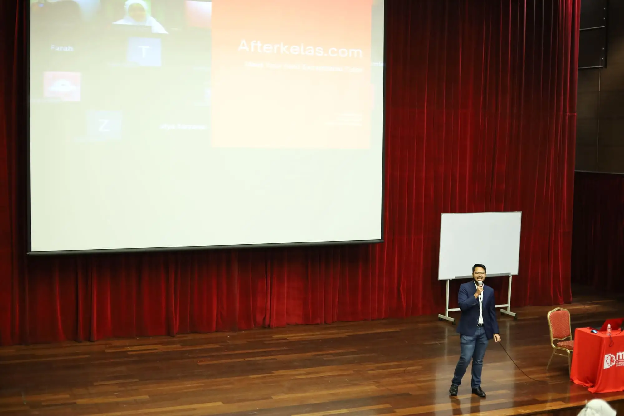 Afterkelas founder Mifzal Salihin on stage beneath a projected Afterkelas.com slide, at a talk for secondary school students in a university hall
